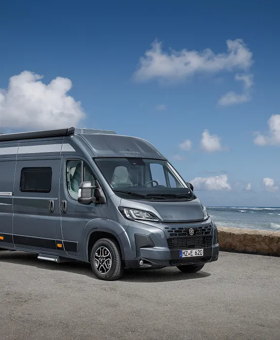 Dunkelgrauer Karmann-Mobil Davis Camper an einer Küstenstraße direkt am Meer unter blauem Himmel. 