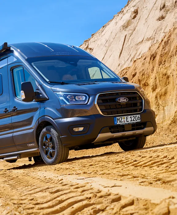 Dunkelgrauer Ford Transit Trail Camper in einer Sandgrube bei strahlend blauem Himmel.